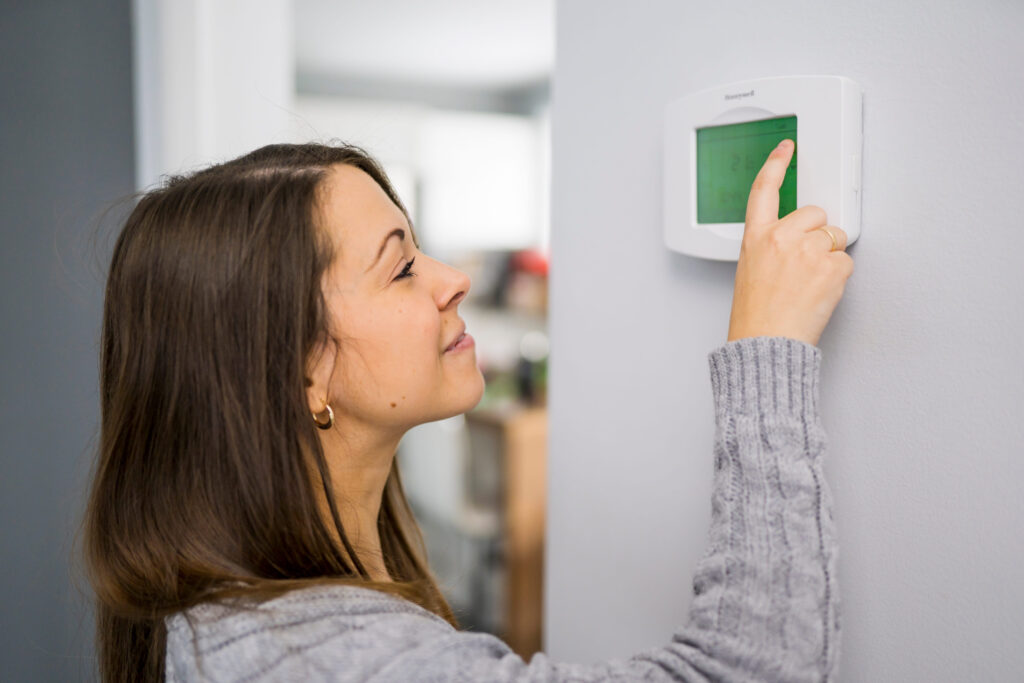 Woman adjusting thermostat for heating and cooling system.