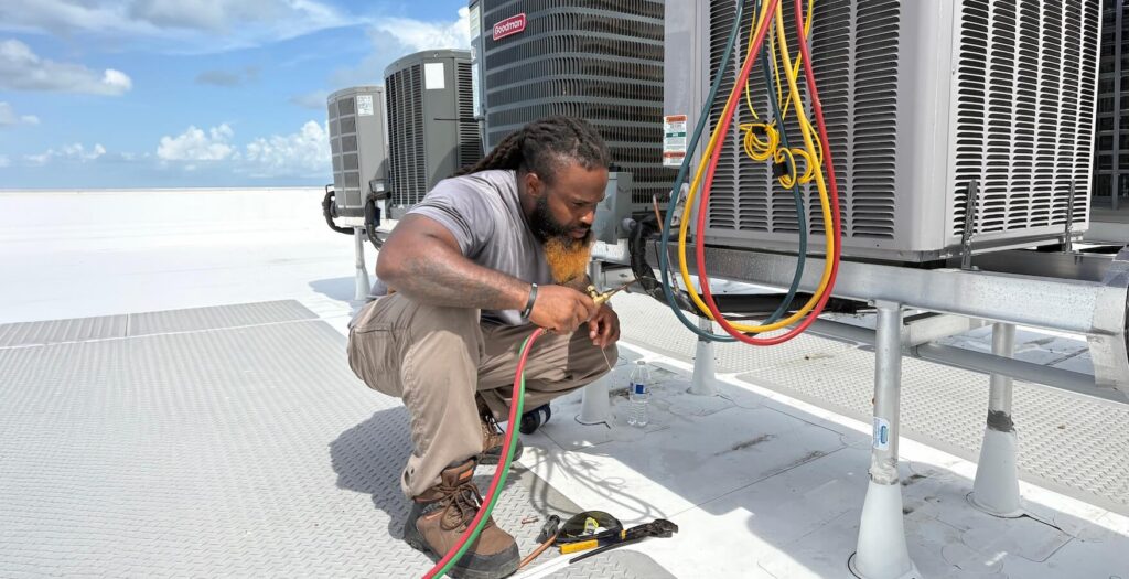 HVAC technician repairing rooftop air conditioning units outdoors.