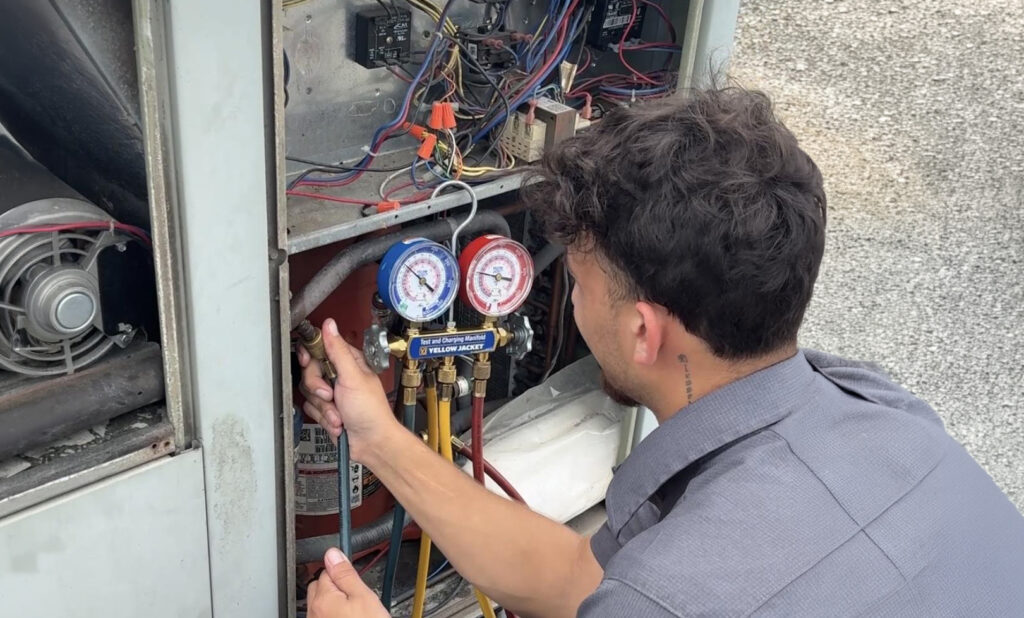 HVAC technician checking refrigerant gauges on an outdoor AC unit.