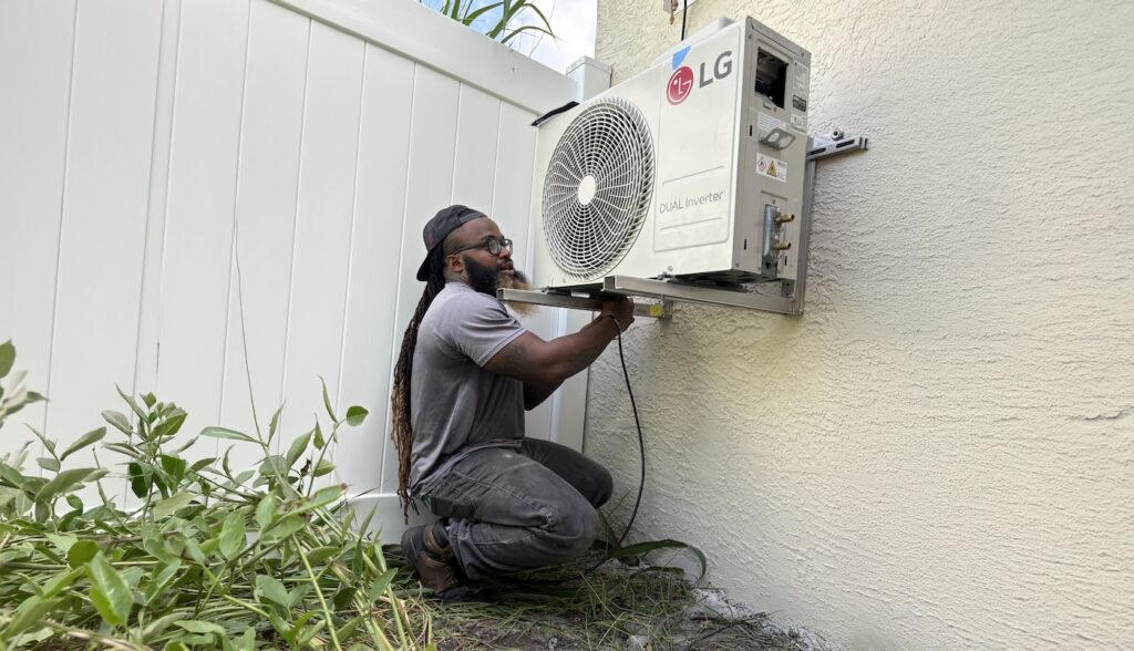 HVAC technician installing outdoor air conditioning unit on house wall.
