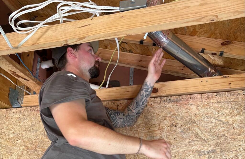 HVAC technician working on ventilation duct in attic space.