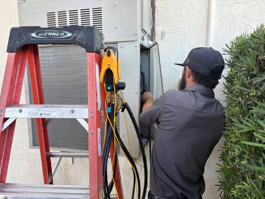 HVAC technician repairing an outdoor cooling system with tools and ladder.